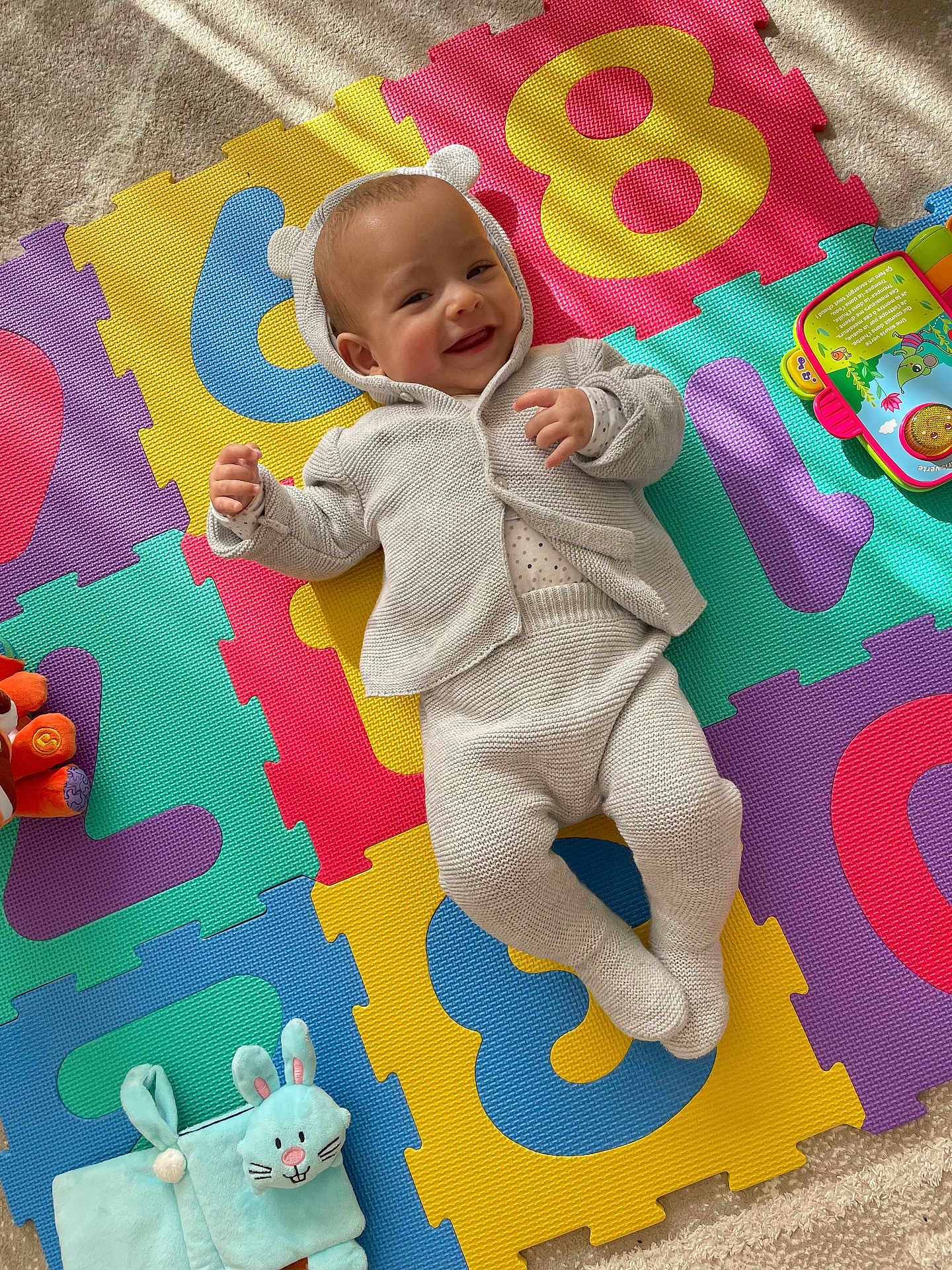 Zayn participe au concours pour gagner de l'argent avec cette photo : baby, infant, child, playmat, numbers, colorful, toy, plush_bunny, smile, face, hooded_sweater, knitted_clothes, carpet, sunlight, shadow, lying_down, playtime, happy, indoor, cute