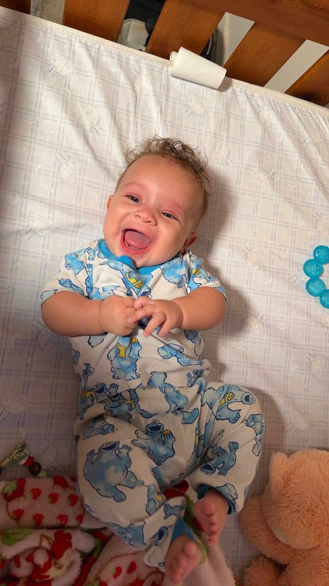 Grayson is registered to the contest to win money with this photo: baby, infant, smiling, pajamas, crib, blanket, plush_toy, teddy_bear, blue, happy, child, cute, lying_down, indoors, face, person, toy, sleepwear, joyful, patterned_clothing