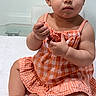 toddler, child, baby, sunglasses, orange_dress, plaid, sitting, indoors, curly_hair, cute, serious_expression, fluffy_surface, skin, earrings, person, portrait, young_child, fashion, accessory, white_background