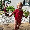 Kashton is registered to the contest to win money with this photo: toddler, child, red_onesie, walking, outdoor, plants, greenery, white_rocks, patio, tiles, building, window, smiling, baby, person, daylight, happy, cute, concrete, foot
