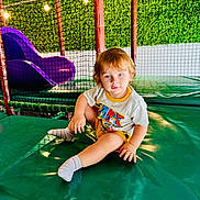 Kenan joined the competition — help win amazing prizes! toddler, child, indoor, play_area, slide, netting, green_wall, padded_surface, socks, shorts, tshirt, blue_eyes, light_hair, playground, lights, seated, cute, smiling, person, casual_clothing