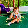toddler, child, indoor, play_area, slide, netting, green_wall, padded_surface, socks, shorts, tshirt, blue_eyes, light_hair, playground, lights, seated, cute, smiling, person, casual_clothing