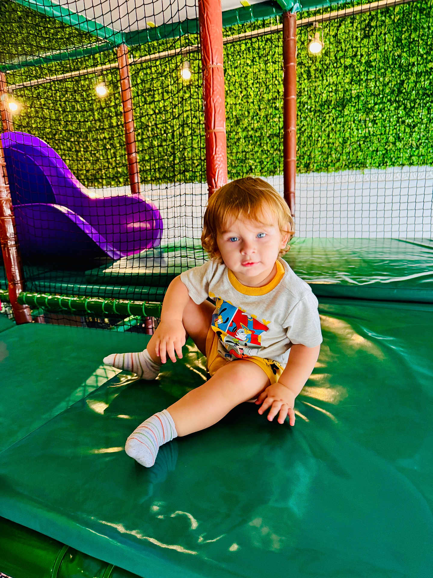 Kenan joined the competition — help win amazing prizes! toddler, child, indoor, play_area, slide, netting, green_wall, padded_surface, socks, shorts, tshirt, blue_eyes, light_hair, playground, lights, seated, cute, smiling, person, casual_clothing