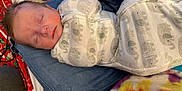 Owen is registered to the contest to win money with this photo: baby, blanket, clothing, cute, denim, elephant_print, fabric, indoor, infant, jeans, lap, newborn, peaceful, person, portrait, red, resting, sleeping, swaddle, tie_dye
