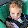 baby, child, car_seat, curly_hair, infant, seatbelt, pink_shirt, straps, safety, serious_expression, closeup, indoors, person, young_child, transportation, warning_label, seat, car_interior, small_hand, portrait