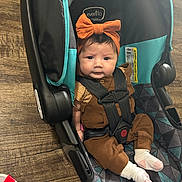 Ruby joined the competition — help win amazing prizes! baby, child, car_seat, headband, orange_bow, brown_outfit, white_socks, flooring, wood_floor, patterned_cushion, seatbelt, straps, drink_cup, red_straw, indoor, infant, cute, portrait, sitting, person