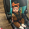 baby, child, car_seat, headband, orange_bow, brown_outfit, white_socks, flooring, wood_floor, patterned_cushion, seatbelt, straps, drink_cup, red_straw, indoor, infant, cute, portrait, sitting, person