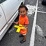 Christopher joined the competition — help win amazing prizes! child, toddler, toy_airplane, orange_apron, parking_lot, car, white_car, black_crocs, asphalt, sidewalk_markings, curly_hair, outdoor, play, expression, person, footwear, clothing, vehicle, daylight, side_view