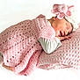 newborn, baby, sleeping, pink, crocheted_blanket, hat, flower, pillow, cozy, resting, infant, cute, soft_texture, smile, peaceful, portrait, child, white_background, hand, clothing