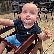 Virgil joined the competition — help win amazing prizes! baby, child, high_chair, food, messy, blue_eyes, navy_shirt, light_blue_shorts, wooden_furniture, restaurant, tiled_floor, curious, tongue_out, indoor, person, seated, table, chair, casual, dining_area