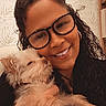 Dolly is registered to the contest to win money with this photo: woman, person, dog, puppy, pet, fluffy, small_dog, cuddle, selfie, portrait, smiling, glasses, curly_hair, long_hair, indoor, wallpaper, furniture, warm_lighting, black_clothing, animal