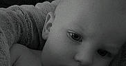 Jacob is registered to the contest to win money with this photo: baby, child, infant, portrait, close_up, face, eyes, serious, lying_down, blanket, couch, indoor, home, black_and_white, grayscale, lock_screen, clock, digital_display, soft_furnishings, photography