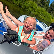 Bowen is registered to the contest to win money with this photo: toddler, woman, inflatable_tube, river, life_vest, tattoo, sunny_day, greenery, smile, snack, outdoor, water, relaxation, summer, nature, happy, floating, family, recreation, casual