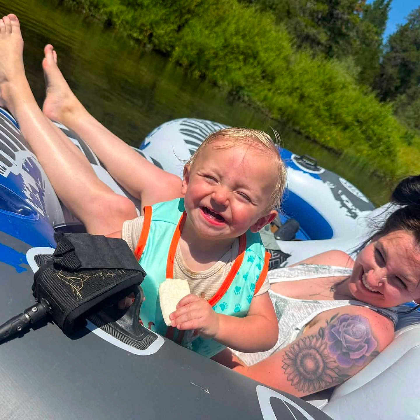 Bowen is registered to the contest to win money with this photo: toddler, woman, inflatable_tube, river, life_vest, tattoo, sunny_day, greenery, smile, snack, outdoor, water, relaxation, summer, nature, happy, floating, family, recreation, casual