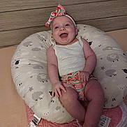 Iris is registered to the contest to win money with this photo: baby, bow, clothing, cushion, cute, foot, hand, happy, headband, indoor, infant, lying_down, person, pink, sheep_pattern, shorts, skin, smile, white, wooden_background