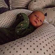 Iris is registered to the contest to win money with this photo: baby, infant, pillow, blanket, green_onesie, heart_pattern, star_pattern, face, resting, cushion, bedroom, sleepwear, soft_lighting, indoors, newborn, comfort, cozy, child, portrait, peaceful
