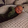 baby, infant, pillow, blanket, green_onesie, heart_pattern, star_pattern, face, resting, cushion, bedroom, sleepwear, soft_lighting, indoors, newborn, comfort, cozy, child, portrait, peaceful