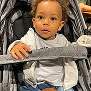 Maylann participe au concours pour gagner de l'argent avec cette photo : toddler, child, stroller, hand, curly_hair, gray_hoodie, blue_pants, safety_bar, indoor, person, seated, baby, expression, support, curiosity, casual_clothing, light, face, portrait, cute