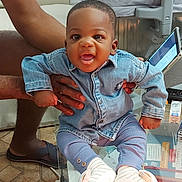 Maël participe au concours pour gagner de l'argent avec cette photo : baby, child, denim_shirt, pants, socks, indoor, glass_table, person, hand, floor, tablet, adult, smiling, seated, casual_clothing, living_room, footwear, toy, expression, furniture