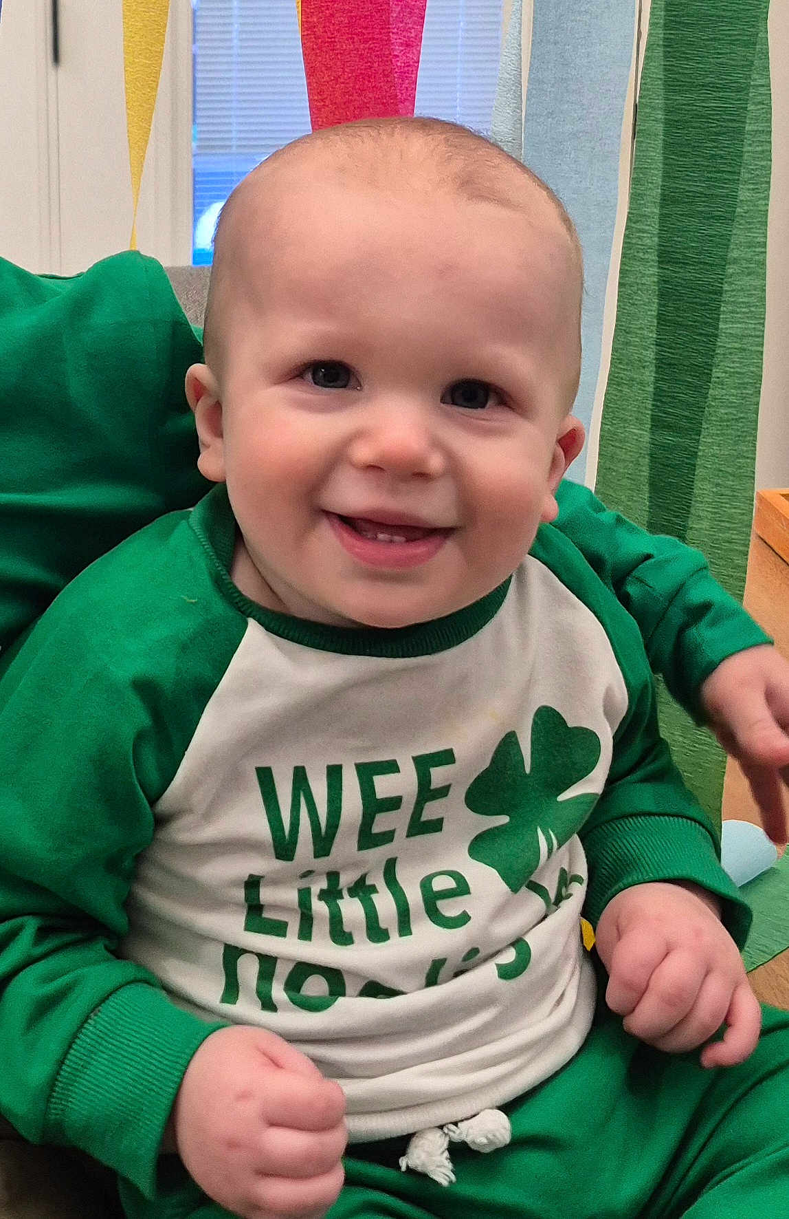 Roman joined the competition — help win amazing prizes! baby, infant, toddler, smiling, face, eyes, teeth, cheeks, onesie, green_clothing, shamrock, st_patricks, portrait, indoor, sitting, hands, party_streamers, cute, happy, clothing
