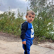 Alessio participe au concours pour gagner de l'argent avec cette photo : blue_clothing, boy, bushes, casual_clothing, child, cloudy_sky, curious_expression, daytime, greenery, nature, outdoor, pathway, person, side_view, sneakers, sportswear, toddler, walking_path, white_shoes, young_child