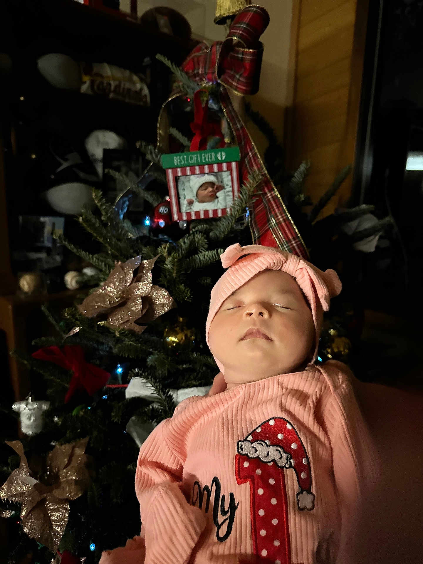 Amelia is registered to the contest to win money with this photo: baby, sleeping, pink_clothing, headwear, christmas_tree, ornaments, holiday_decor, indoor, festive, portrait, child, soft_lighting, celebration, holiday_season, infant, cute, cozy, family, seasonal, decorations