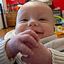 baby, bib, child, close_up, cozy, cute, face, furniture, hand, happy, indoor, person, portrait, red_wall, room, skin, smile, sweater, wooden_drawer, young_child