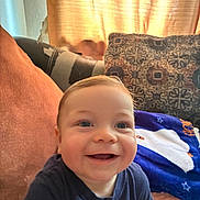 Nicolas is registered to the contest to win money with this photo: baby, smiling, child, couch, pillow, blanket, indoor, happy, face, blue_shirt, curtain, light, cozy, home, infant, seated, cheerful, portrait, young_child, comfort