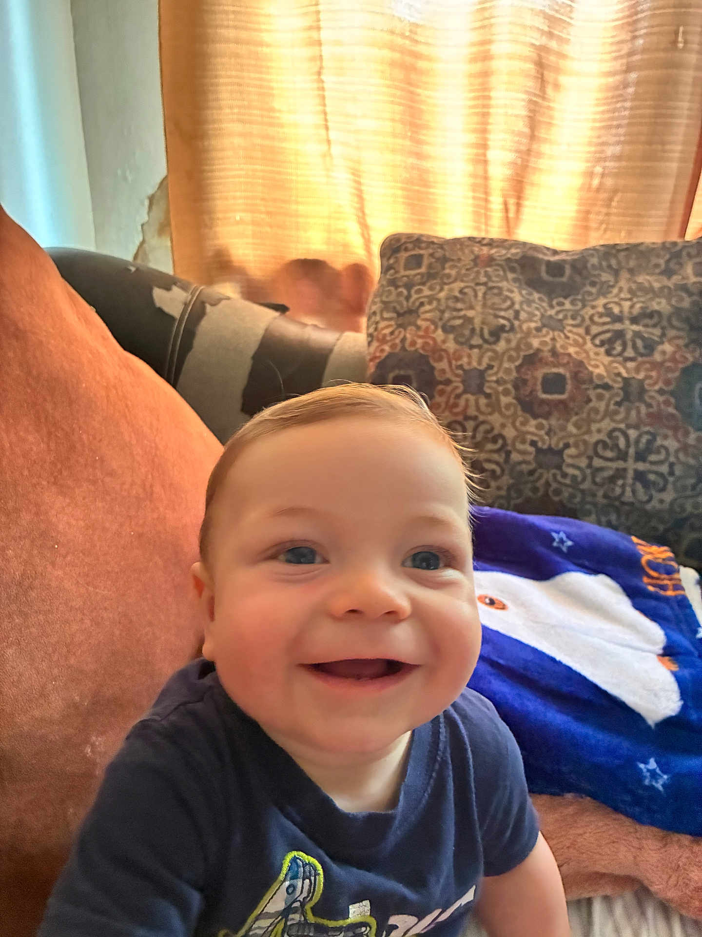 Nicolas is registered to the contest to win money with this photo: baby, smiling, child, couch, pillow, blanket, indoor, happy, face, blue_shirt, curtain, light, cozy, home, infant, seated, cheerful, portrait, young_child, comfort
