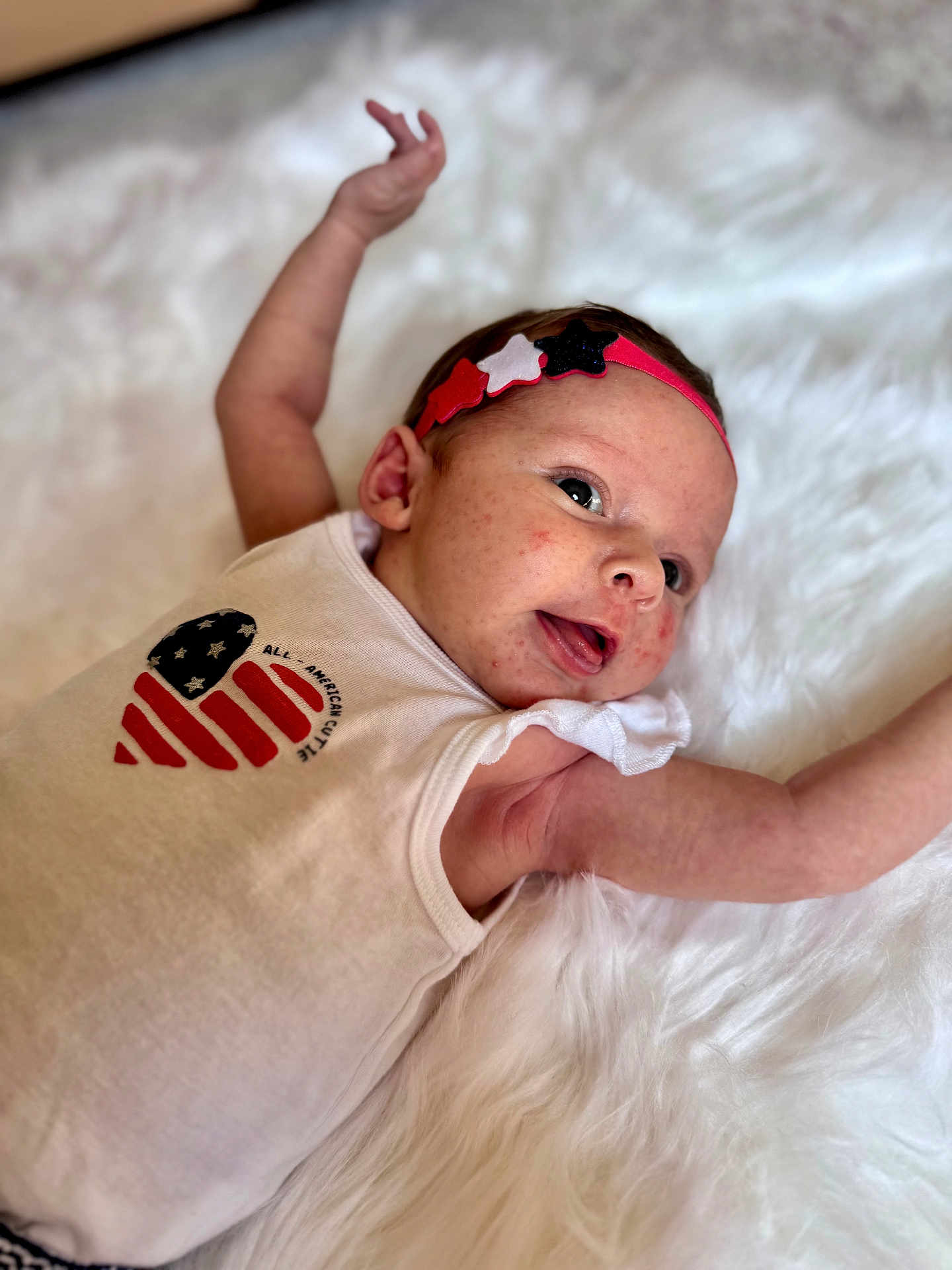 Elliana is registered to the contest to win money with this photo: baby, infant, headband, stars, white_background, sleeveless_shirt, patriotic, heart_design, arms_outstretched, cute, lying_down, skin_detail, happy_expression, soft_texture, closeup, portrait, child, newborn, fluffy_surface, casual_clothing