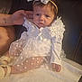 Aaliyah participe au concours pour gagner de l'argent avec cette photo : baby, infant, white_dress, bow_headband, floral, cute, soft_blanket, tattoo, adult_hand, leather_couch, sitting, portrait, indoors, curious_expression, child, footwear, long_sleeves, headwear, person, closeup