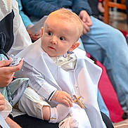 Maneo a rejoint le concours — aidez-le/la à gagner de superbes lots ! baby, child, christening, cross, white_clothing, socks, indoor, people, seated, holding, religious, event, curious, portrait, infant, hands, face, person, paper, background