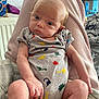 Enzo-John is registered to the contest to win money with this photo: baby, infant, onesie, dinosaur_print, legs, indoor, blanket, person, face, curious, pout, casual, clutter, soft_lighting, home, seated, young_child, skin, head, expression