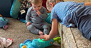 Oliver joined the competition — help win amazing prizes! child, baby, toddler, toy, carpet, couch, pajamas, indoor, play, curtains, cushions, striped_shirt, floor, furniture, window_light, room, interaction, colorful_toy, young_child, home