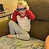 Oliver is registered to the contest to win money with this photo: child, boy, sunglasses, couch, blanket, indoor, casual_clothing, red_shirt, gray_pants, barefoot, smiling, seated, home, furniture, table, remote_control, toy, relaxed, cute, playful