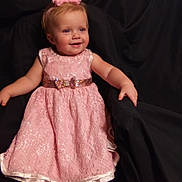 Lyra is registered to the contest to win money with this photo: toddler, girl, pink_dress, headband, smile, child, portrait, happy, seated, lace, sparkle, indoor, cute, baby, fashion, person, cloth, background, black_fabric, chubby_cheeks
