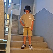 Alessio participe au concours pour gagner de l'argent avec cette photo : boy, bucket_hat, casual, child, confident, door, fashion, hand_on_hip, hat, indoor, pose, shorts, sneakers, stairs, standing, sunglasses, tile_floor, tshirt, wall, window
