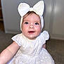 apparel, baby, bow, child, cute, expression, eyes, face, fashion, happy, headband, indoor, infant, person, portrait, sitting, skin, smiling, white_dress, young