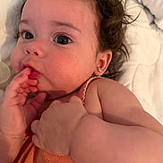 Athena joined the competition — help win amazing prizes! baby, child, close_up, curly_hair, cute, earrings, expression, face, fingers, infant, innocence, laying_down, orange_clothing, person, portrait, skin, soft_blanket, sucking_fingers, toddler, young_child