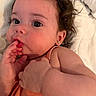 baby, child, close_up, curly_hair, cute, earrings, expression, face, fingers, infant, innocence, laying_down, orange_clothing, person, portrait, skin, soft_blanket, sucking_fingers, toddler, young_child