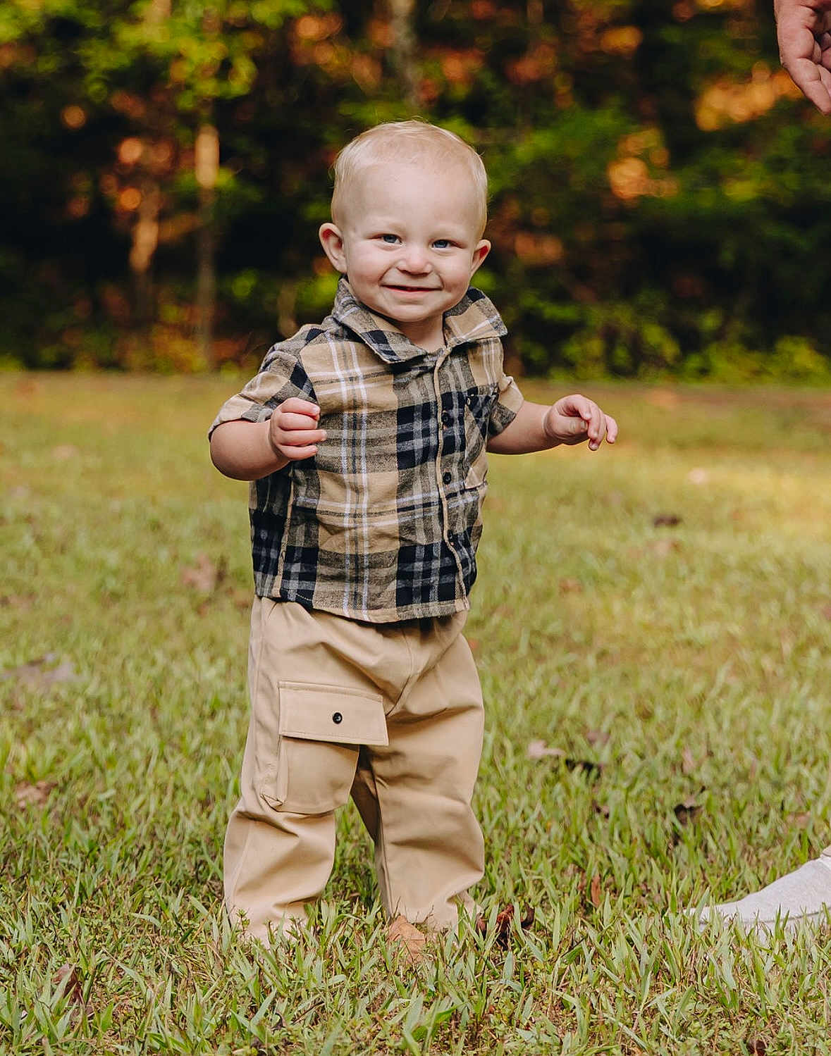 Dallas Kash is registered to the contest to win money with this photo: toddler, child, smiling, grass, outdoor, plaid_shirt, beige_pants, person, nature, happy, cute, standing, baby, portrait, feet, hand, casual_clothing, daylight, greenery, young