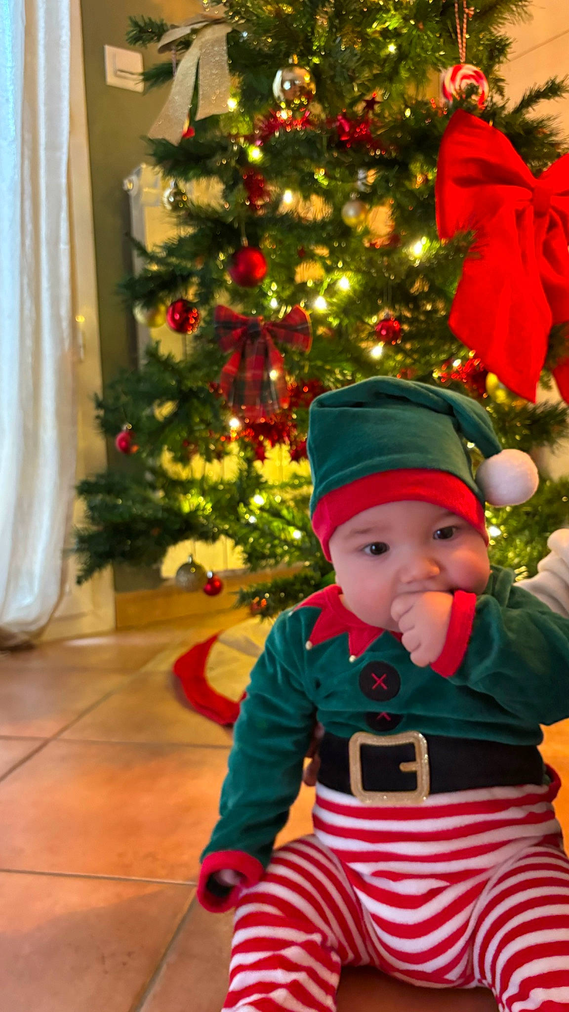 Tom participe au concours pour gagner de l'argent avec cette photo : baby_toddler_clothing, christmas, christmas_decoration, christmas_eve, christmas_ornament, christmas_tree, costume_hat, curtain, event, evergreen, happy, hat, headwear, holiday, holiday_ornament, ornament, person, red, sleeve, toddler