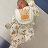 baby, newborn, infant, lying_down, onesie, bib, hat, animal_print, giraffe, cute, expression, medical_table, scrunched_face, clothing, sleepwear, child, person, indoors, newborn_baby, adorable