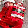 baby, sleeping, red_outfit, hat, gift, present, cushion, patterned_blanket, infant, hand, face, cozy, holiday, christmas, soft_texture, cute, resting, indoors, child, wrapped_present