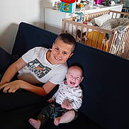 Eliott participe au concours pour gagner de l'argent avec cette photo : child, baby, smiling, laughing, couch, indoor, crib, toy, nursery, furniture, happy, person, clothing, home, sitting, family, brother, infant, casual, relaxing