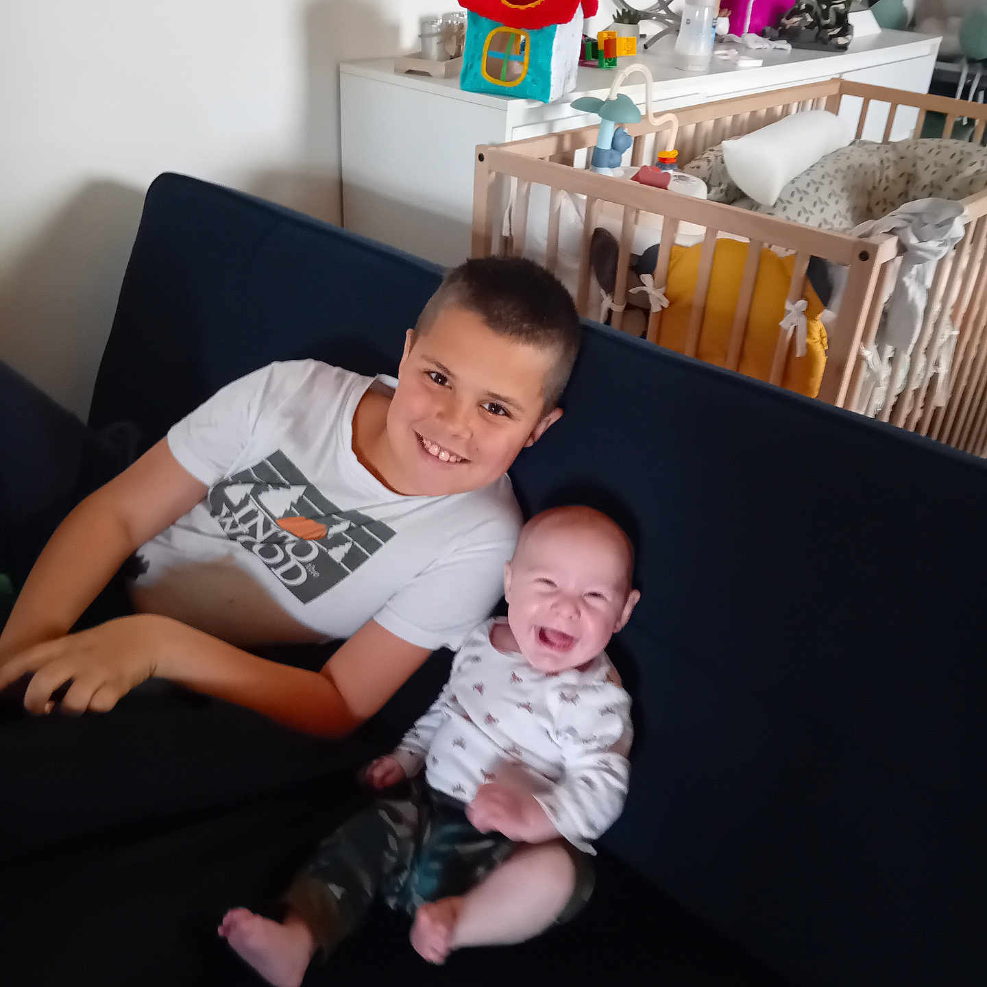 Eliott participe au concours pour gagner de l'argent avec cette photo : child, baby, smiling, laughing, couch, indoor, crib, toy, nursery, furniture, happy, person, clothing, home, sitting, family, brother, infant, casual, relaxing