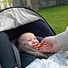 baby, smiling, stroller, jacket, hand, biscuit, outdoor, grass, wall, person, child, blanket, happy, infant, seat, cozy, feeding, cute, nature, playful