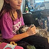 cat, gray_cat, pet, person, child, girl, indoor, sitting, lap, belly_up, tummy_rub, fluffy, fur, whiskers, eyes, pink_shirt, luggage, window, backpack, household