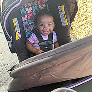 Imanii joined the competition — help win amazing prizes! baby, child, infant, smiling, car_seat, stroller, harness, outdoor, portrait, face, brown_hair, pink_shirt, butterflies, sunlight, pavement, fabric, safety_straps, cup, yellow_liquid, happy