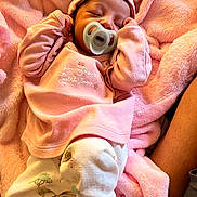 Imanii is registered to the contest to win money with this photo: baby, newborn, pacifier, pink_blanket, headband, sleeping, infant, soft_fabric, cozy, cute, child, clothing, nap, resting, indoors, toddler, person, closeup, warm_colors, comfort
